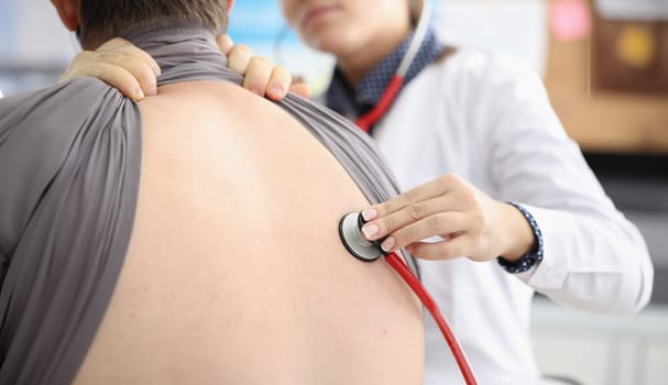 Female doctor listens to man back through astethoscope. Inflammation of lungs and painful cough