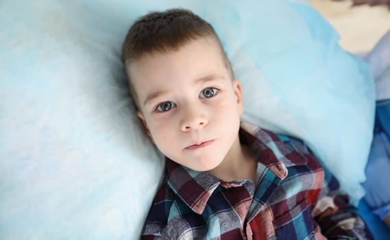 Portrait of cute little boy in colored shirt looking at camera with serious attentive face. Calm thoughtful facial expression concept