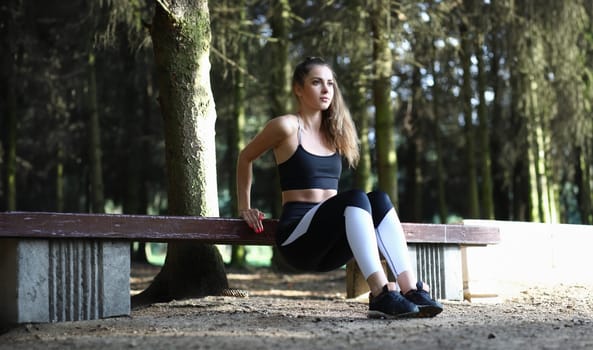 Female trainer goes in for sports outdoors in park. Athlete doing favorite work of squats for health