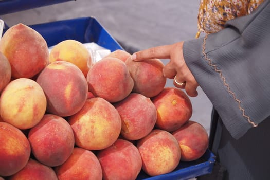 A hand carefully selects ripe and juicy peaches from a vibrant and colorful market display