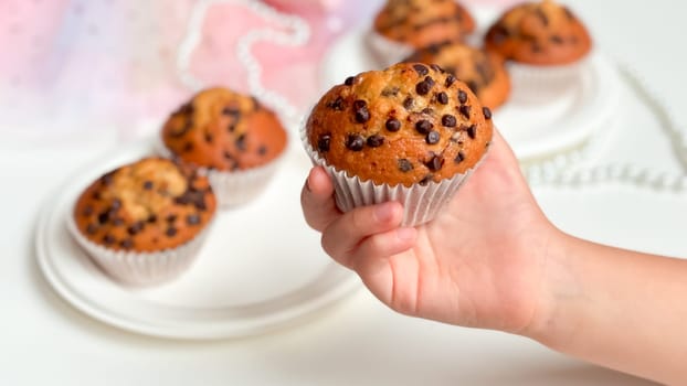 Childs hand holding chocolate chip muffin with delicious treats in background. Birthday concept.