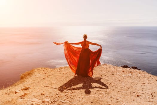 Woman red dress sea. Female dancer in a long red dress posing on a beach with rocks on sunny day. Girl on the nature on blue sky background