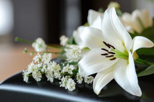 A combination of white lilies and small delicate flowers is thoughtfully placed on a dark surface, creating a poignant tribute at a funeral setting, symbolizing remembrance and peace.