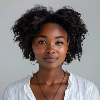 A woman with black hair styled in ringlet curls is wearing a white shirt and hoop earrings. Her smile shows off her cool hoop earrings and necklace