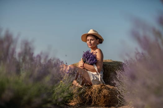 A woman is sitting in a field of lavender flowers and wearing a straw hat. She is smiling and holding a bouquet of flowers. Scene is peaceful and serene, as the woman is surrounded by the beauty of nature.