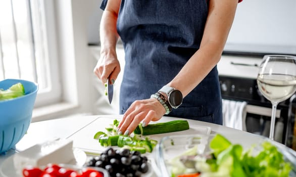 Woman At Home In Kitchen Cuts Cucumbers Preparing Greek Salad