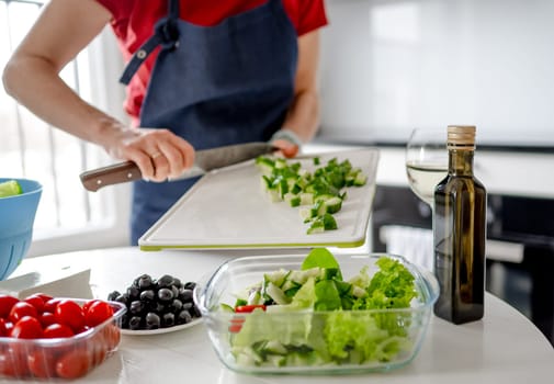 Girl Pours Chopped Cucumbers Into Bowl For Greek Salad At Home In Bright Kitchen