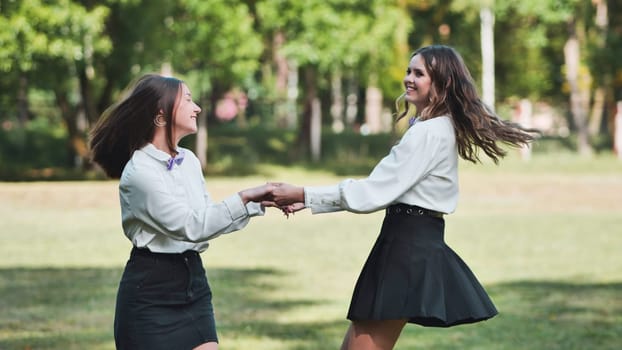 Two happy schoolgirls holding hands and spinning around in the park, enjoying their first day back at school