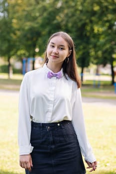 Portrait of a smiling student girl wearing a purple bow tie and posing in a park on her first day of school