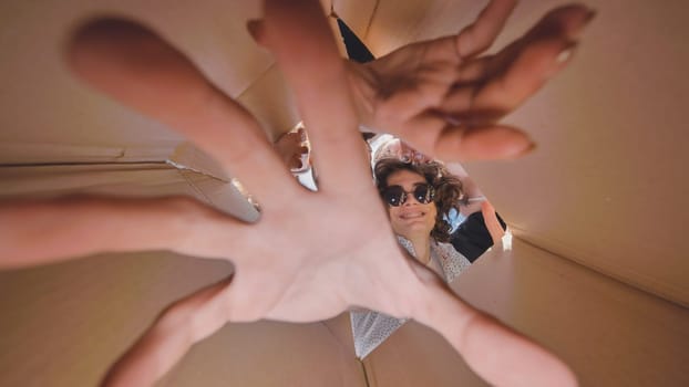 Group of teenagers enjoying playful moments inside a cardboard box, reaching out with smiles, embodying joy and carefree summer fun