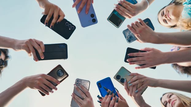 Group of high school students holding smartphones forming a circle against a blue sky on a summer day