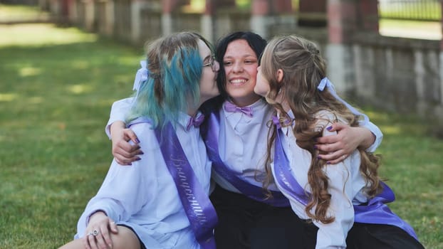 Three graduates celebrating their graduation by kissing their classmate on the cheeks during their last day of school