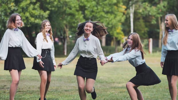 Five cheerful schoolgirls running together in the park, holding hands and celebrating their first school day