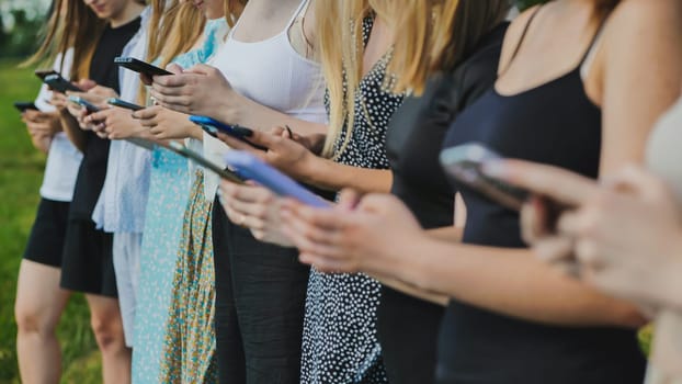 Group of students using smartphones outdoors in the summer, concept of technology addiction and social media