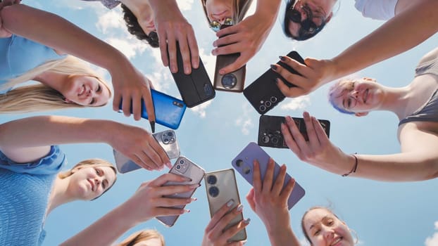 Group of teenage girls holding smartphones making a circle shape with their mobile phones against the blue sky