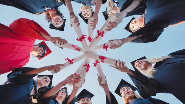 Group of cheerful graduates wearing caps and gowns forming a circle with their diplomas in their hands