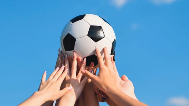 Group of friends holding a soccer ball over their heads against a clear blue sky, symbolizing teamwork and friendship