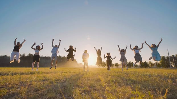 Group of friends are joyfully jumping in a field, silhouetted against the warm glow of the setting sun, celebrating their graduation