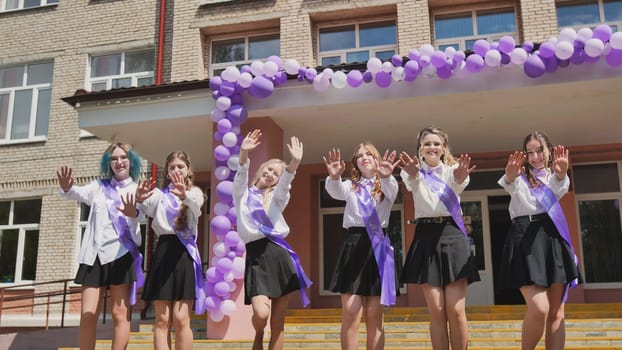 Group of cheerful graduates waving goodbye on their last school day, celebrating the end of the academic year with purple ribbons and balloons