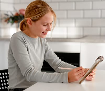 Happy, Cute Little Girl Writes A To-Do List In Notebook At Home