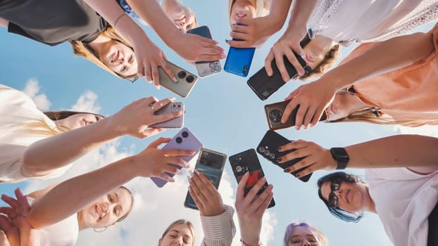 Group of teenagers making circle with smartphones on background of blue sky, taking photo of themselves on their phones, concept of modern communication