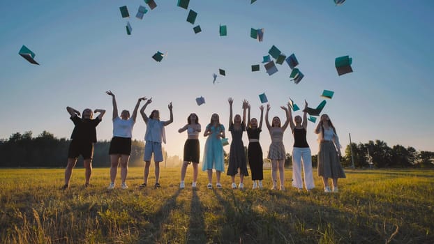 High school students joyfully tossing books in the air to celebrate the start of summer vacation in a field at sunset
