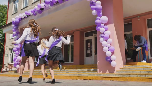 Schoolgirls happily running out of school after graduation, celebrating end of year with purple ribbons and festive decorations, looking forward to summer break and bright future ahead
