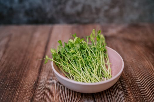 Young green sprouts of microgreen peas lie in a pink plate on a wooden table. High quality photo