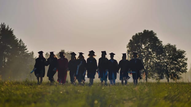 Six graduates in robes walk against the backdrop of the sunset.