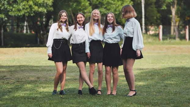 Five cheerful high school students wearing white shirts and bow ties are enjoying their first day back at school together in a park