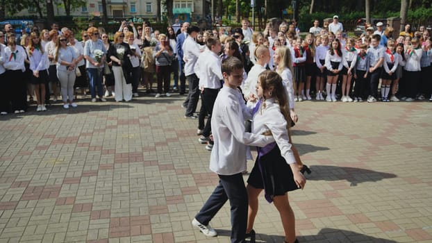 Teenage students dancing waltz at their last school day ceremony in the schoolyard, with teachers and parents watching and taking pictures