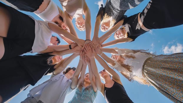 Group of high school students forming a circle, joining their hands together against a bright blue sky, symbolizing teamwork, unity, and collaboration