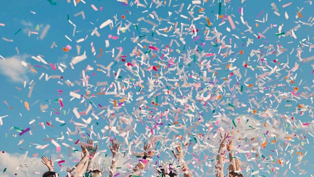 Group of cheerful high school students throwing colorful confetti into the air, celebrating their graduation under a bright blue sky