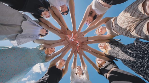 Group of high school students forming a circle with their hands together, enjoying their summer vacation and the power of friendship against a clear blue sky