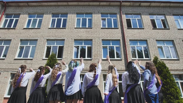 Group of graduating students waving goodbye to their school building on their last day, celebrating the end of an era