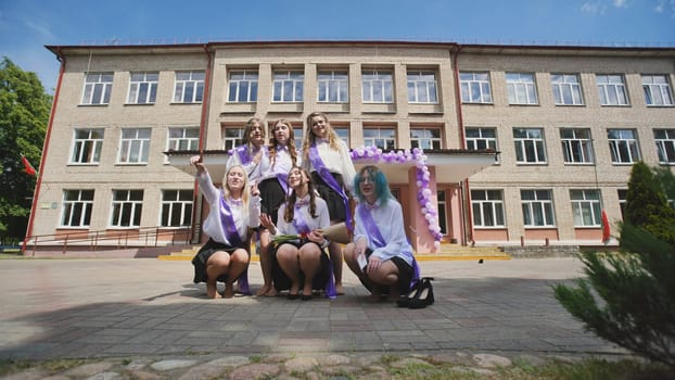 Group of happy female graduates wearing sashes celebrating their last school day in front of the school building