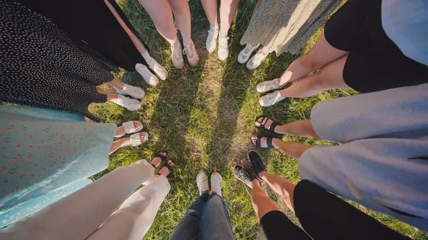 Diverse group of friends standing in a circle on lush green grass, enjoying a sunny summer day. They wear casual clothes and various shoes, radiating happiness and friendship
