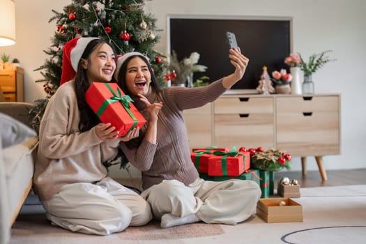 A young woman couple joyfully exchanges a surprise gift box on Christmas Day, capturing the festive spirit in a cozy home environment.