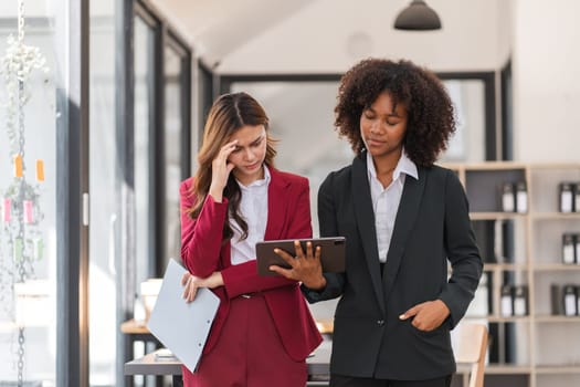 Businesswoman experiencing stress at work while discussing tasks with a colleague in a modern office setting.