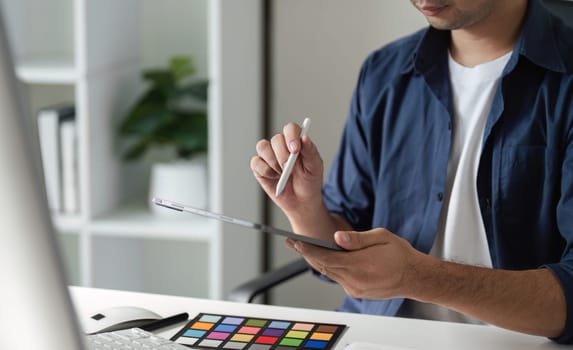 Graphic designer using a tablet and color palette to choose vibrant colors for a digital design project in a modern workspace.