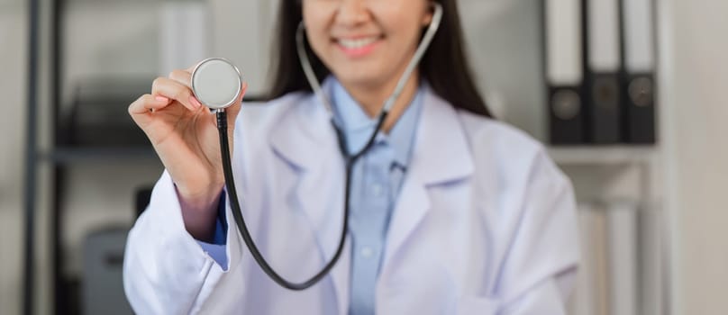 Confident female doctor in a white coat holding a stethoscope, symbolizing professionalism and expertise in a modern medical office.