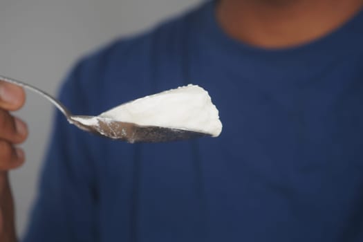 A spoonful of creamy yogurt is held by a person against a neutral background, exuding elegance