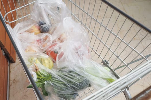 A grocery cart full of vibrant, fresh fruits and wholesome vegetables in clear bags