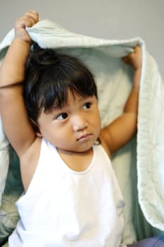 Child playing hiding under the blanket on a bed.