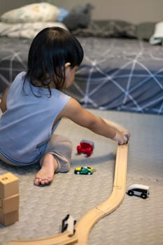 Little boy in a blue shirt sits on the floor playing with a blue train on a wooden track. Education concept.