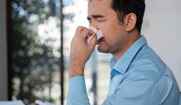 Office worker experiencing cold symptoms, looking unwell at their desk in a modern office setting.
