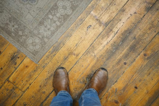 Closeup of stylish brown boots on a rustic wooden floor beside a decorative area rug