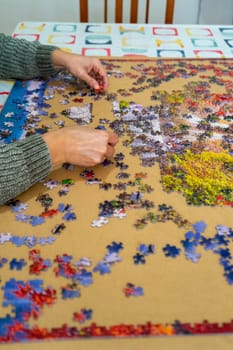 Female hands collect scattered puzzles on a brown background. Board games, hobby, leisure. Entertainment concept.