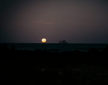 Early sunrise or sunset over the ocean, beach with black volcanic sand at dusk in the darkness the first ray.
