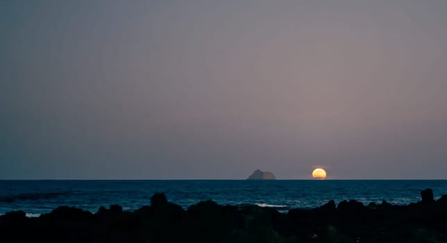 Early sunrise or sunset over the ocean, beach with black volcanic sand at dusk in the darkness the first ray.